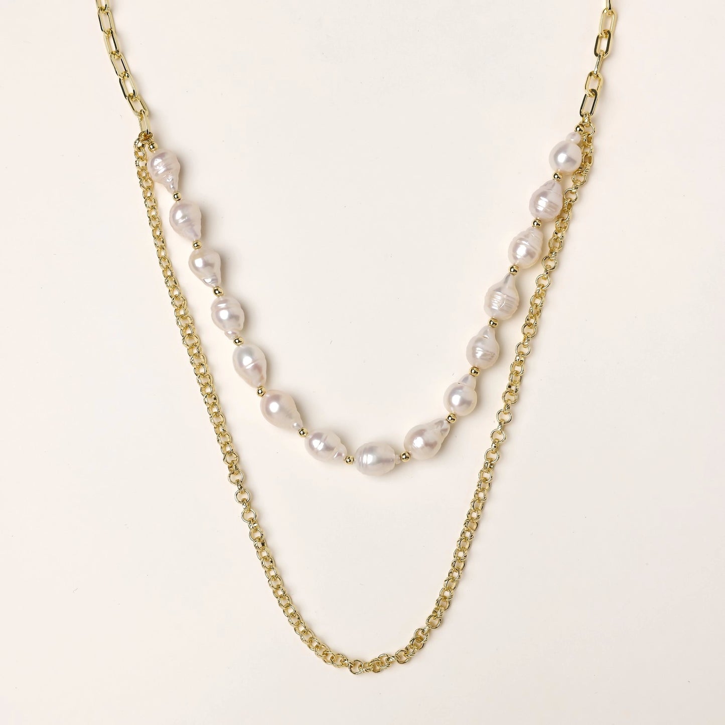 Layered gold chain necklace with organic baroque freshwater pearls and adjustable length on cream background