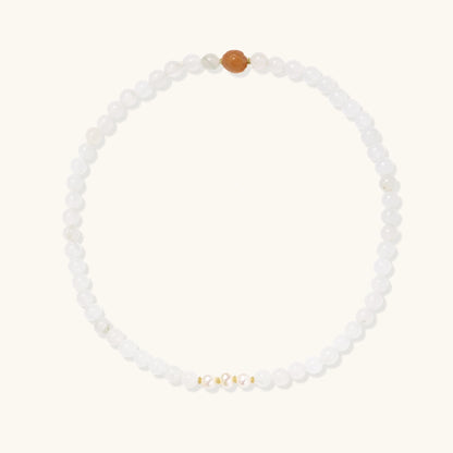 Three layered white beaded bracelets with carved orange agate lotus centerpiece and freshwater pearls on cream background.
