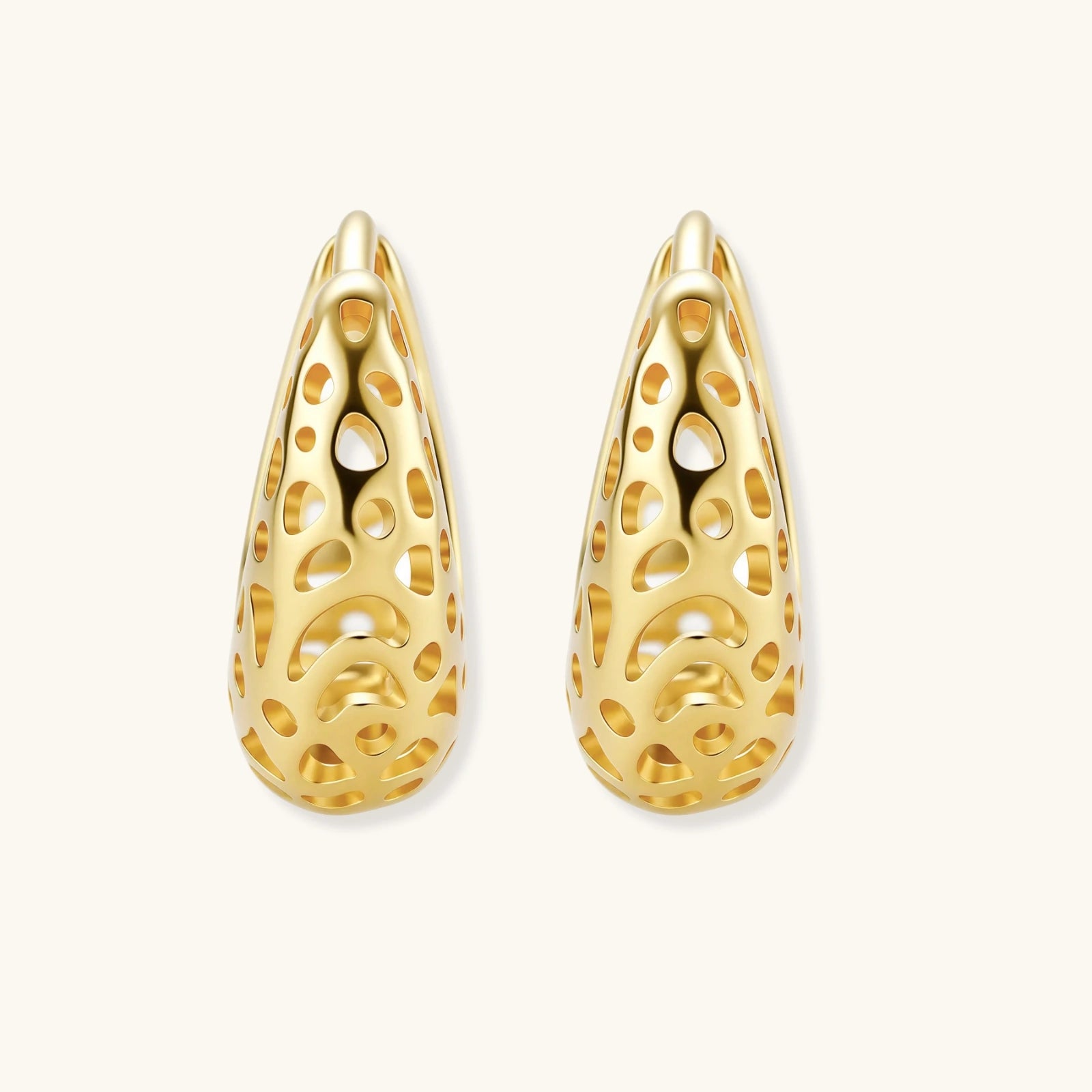 Close-up of small gold-plated hoop earrings with intricate honeycomb cutout pattern on cream background.