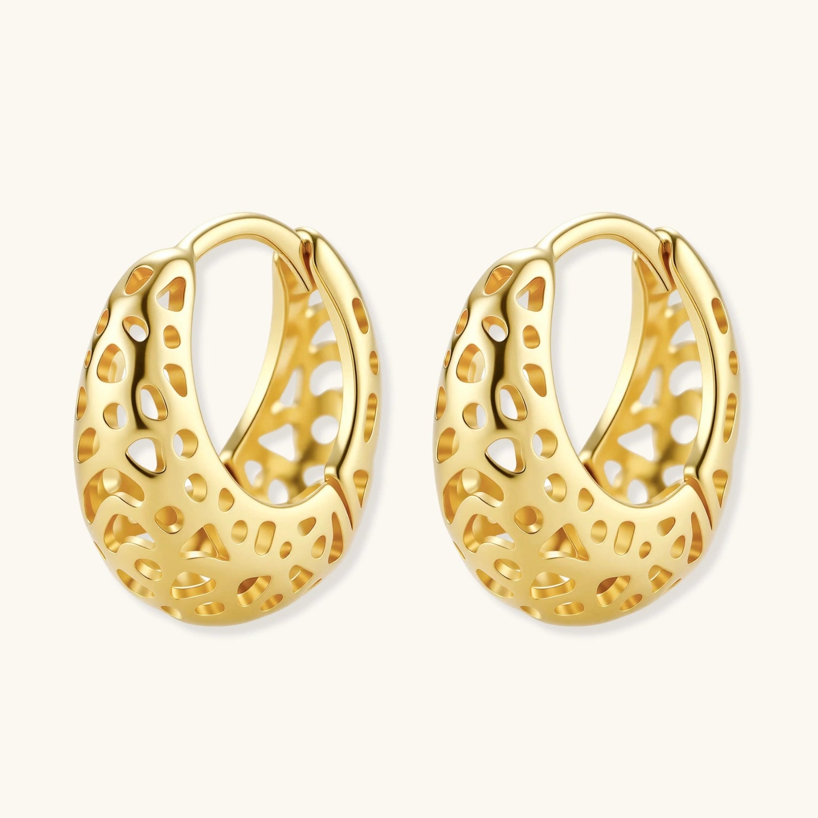 Close-up of small gold-plated hoop earrings with intricate honeycomb cutout pattern on cream background.