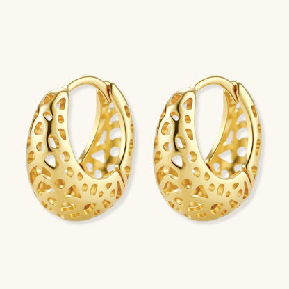 Close-up of small gold-plated hoop earrings with intricate honeycomb cutout pattern on cream background.