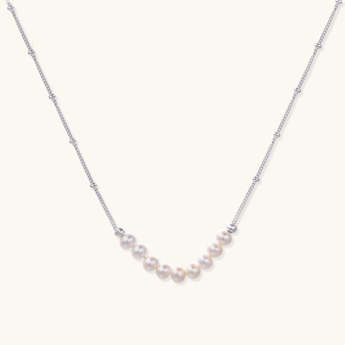 Delicate sterling silver chain necklace with small freshwater pearls arranged in a curved smile arc on cream background.