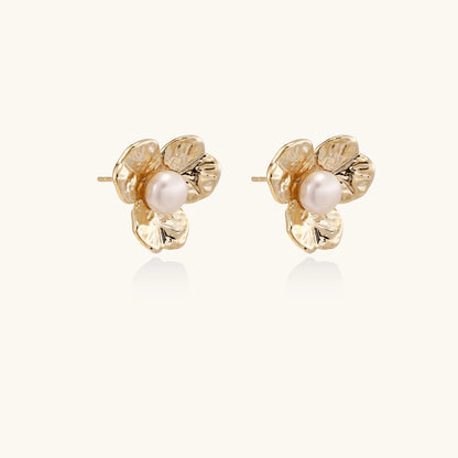 Gold-plated flower stud earrings with textured petals and centered freshwater pearl on beige background